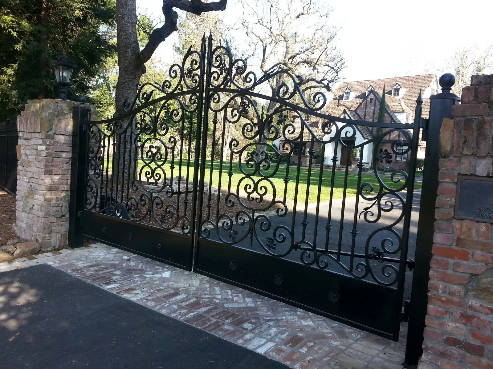 A wrought iron gate is open to a driveway leading to a house