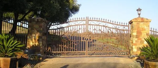 A large metal gate is surrounded by trees and potted plants