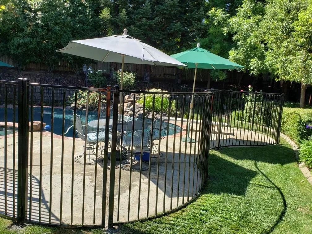 A black metal fence surrounds a patio area with umbrellas and tables